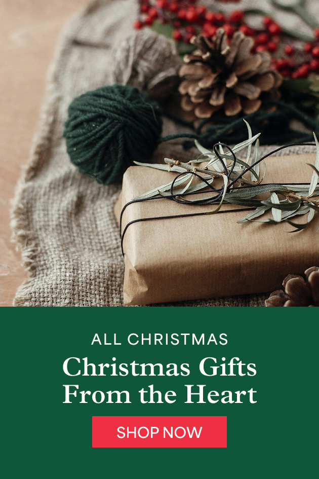 A gift wrapped in brown paper and twine, with a pinecone, red berries and green yarn on burlap. All Christmas. Christmas gifts from the heart. Shop now.