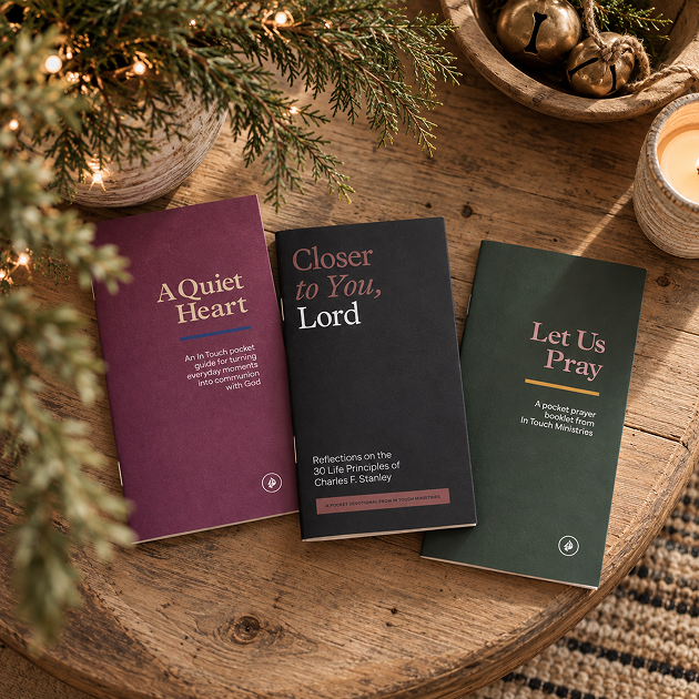 Three pocket booklets, A Quiet Heart, Closer to You, Lord, and Let Us Pray, on a wooden board with greenery and a candle.