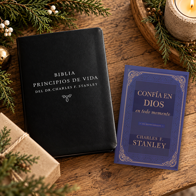 La Biblia Principios de Vida del Dr. Charles F. Stanley y el devocional Confía en Dios en todo momento, con ramas de pino y un regalo envuelto.